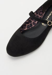 Čierna semišová Mary Jane topánka s okrúhlou špičkou, tenkým remienkom, zlatou kovovou súčasťou a podšívkou s leopardím vzorom. Hladká textúra s jednoduchým dizajnom.