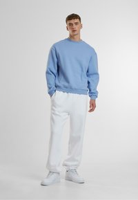 Lichtblauwe sweatshirt met ronde hals, ontspannen pasvorm, van katoen. Gecombineerd met witte joggingsbroek, met elastische cuffs en witte sneakers.