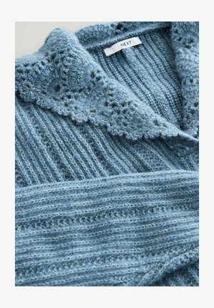 Hele sinine kudumine sviiter, millel on laineline krae, ribakudumise tekstuur ja kihilised kangaste üksikasjad. Brändi silt on nähtav kaela juures.