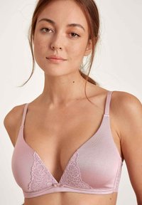 Lichtroze driehoekige bralette gemaakt van een zachte stof, met kantaccenten en verstelbare bandjes, voorzien van een delicate strik in het midden.