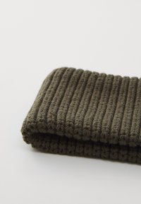 Knitted olive green scarf with a ribbed texture, folded to show the thickness and pattern of the fabric.