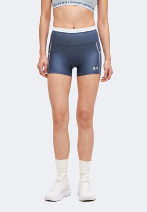 A nő tengerészkék, testhezálló sport rövidnadrágot visel, fehér Under Armour logóval, fehér zoknival, fehér sportcipővel és szürke sportmelltartóval.