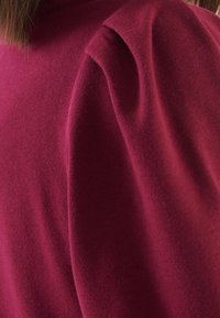 Burgundy stickad tröja med rundad halsringning och puffärmsdetalj, som visar en mjuk textur och en åtsittande passform.