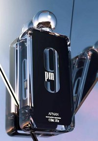 Svart rektangulär parfymflaska med ett silverfärgat runt lock. Etiketten visar "9 pm" med fet vit text. Slank glasdesign med reflekterande ytor.