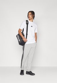 Λευκό μπλουζάκι Adidas με μαύρο λογότυπο, γκρι φόρμες με μαύρες ρίγες, μαύρο σακίδιο πλάτης με λευκό λογότυπο και μαύρα αθλητικά παπούτσια.