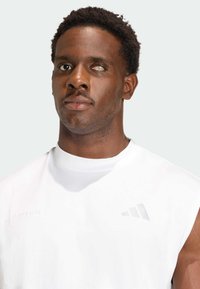 Valkoinen hihaton urheilupaita pyöreällä pääntiellä, hienovarainen vaaleanharmaa logo, valmistettu sileästä kankaasta, sopii juoksuun.