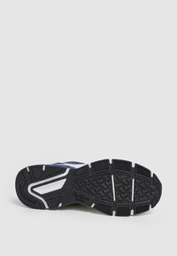 Suela de goma negra de una zapatilla con un patrón de textura en la suela, con un upper en color marino y acentos blancos. Marca de Pepe Jeans visible.