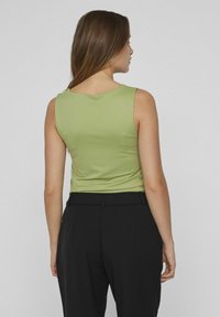 Beżowa top bez rękawów z jasnej tkaniny, z okrągłym dekoltem i dopasowanym krojem. W połączeniu z czarnymi spodniami o wysokim stanie. Gładka tekstura.