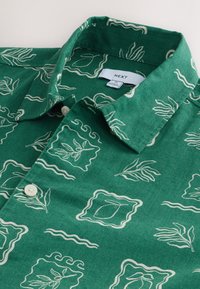 Green button-up shirt featuring a linen-like texture with a cream abstract leaf print and wavy lines, finished with a folded collar.
