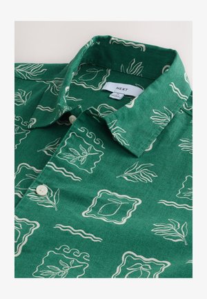 Camicia verde con bottoni, caratterizzata da una texture simile al lino con una stampa astratta a foglie color crema e linee ondulate, rifinita con un colletto piegato.