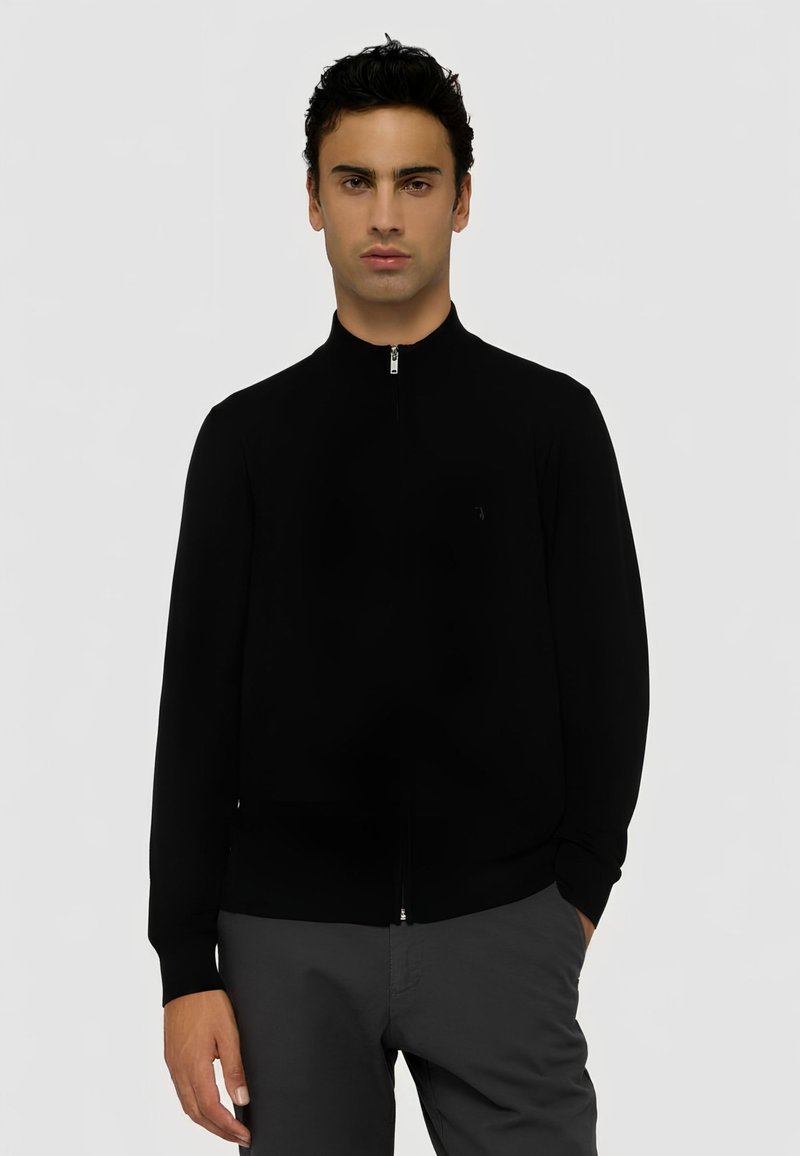 Černý zipový svetr s vysokým límcem, přiléhavým střihem, dlouhými rukávy a jemným logem na hrudi. Texturovaná tkanina.