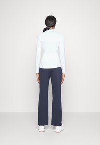 White long-sleeve top paired with navy wide-leg pants and white sneakers, showcasing a fitted design and smooth texture.
