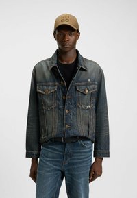 Jeansjacka med mörk tvätt, med knäppning fram, två bröstfickor och kontrasterande sömmar. Matcher med en svart skjorta och blå jeans.