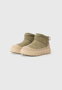 Gröna mockakängor till anklarna med en beige gummisula, rundad tå och en uppvikt design. Har en baksida dragflik för enkel påtagning.