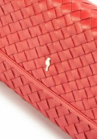 Czerwony pleciony skórzany kopertówka o gładkiej teksturze, z dodatkiem złotego akcentu w postaci ptaka oraz ukośnymi detalami przeszyć.