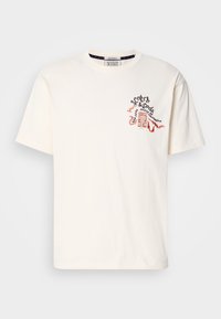 Κρέμα μπλουζίτσα φτιαγμένη από βαμβάκι. Διαθέτει μια πολύχρωμη κεντητή σχεδίαση στο στήθος με κείμενο και μοτίβο κτιρίου. Βραχίονες κοντοί.