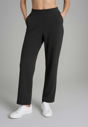 Pantaloni neri a vita alta con gamba larga e tasche laterali, realizzati in tessuto morbido, abbinati a sneakers bianche con lacci.