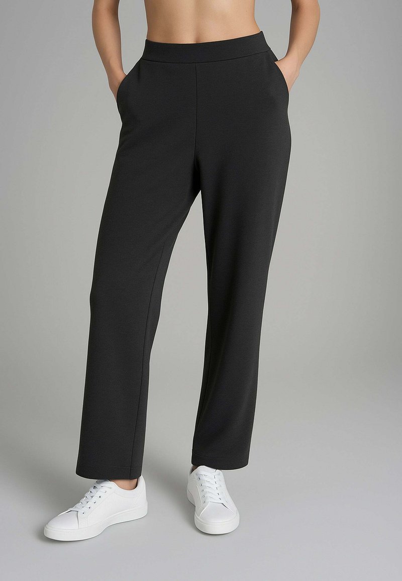 Pantaloni neri a vita alta con gamba larga e tasche laterali, realizzati in tessuto morbido, abbinati a sneakers bianche con lacci.