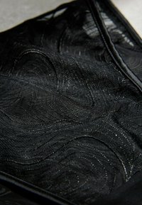 Schwarzer, durchscheinender Stoff mit wirbelnden, strukturierten Mustern und leicht glänzender Oberfläche, gefaltet mit sichtbaren Kanten und Nähten.