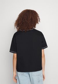 T-shirt nera a maniche corte realizzata in tessuto liscio, con piping bianco lungo il collo e le maniche, mostrata da dietro su uno sfondo neutro.