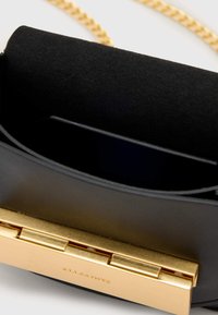 Borsa in pelle nera con interni in suede, chiusura in metallo dorato e tracolla a catena. Presenta un solo scomparto e una finitura liscia.