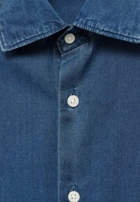 Blauer Denim-Hemdkragen und Vorderseite mit drei weißen Knöpfen, die detaillierte Nähte und Stoffstruktur zeigen.