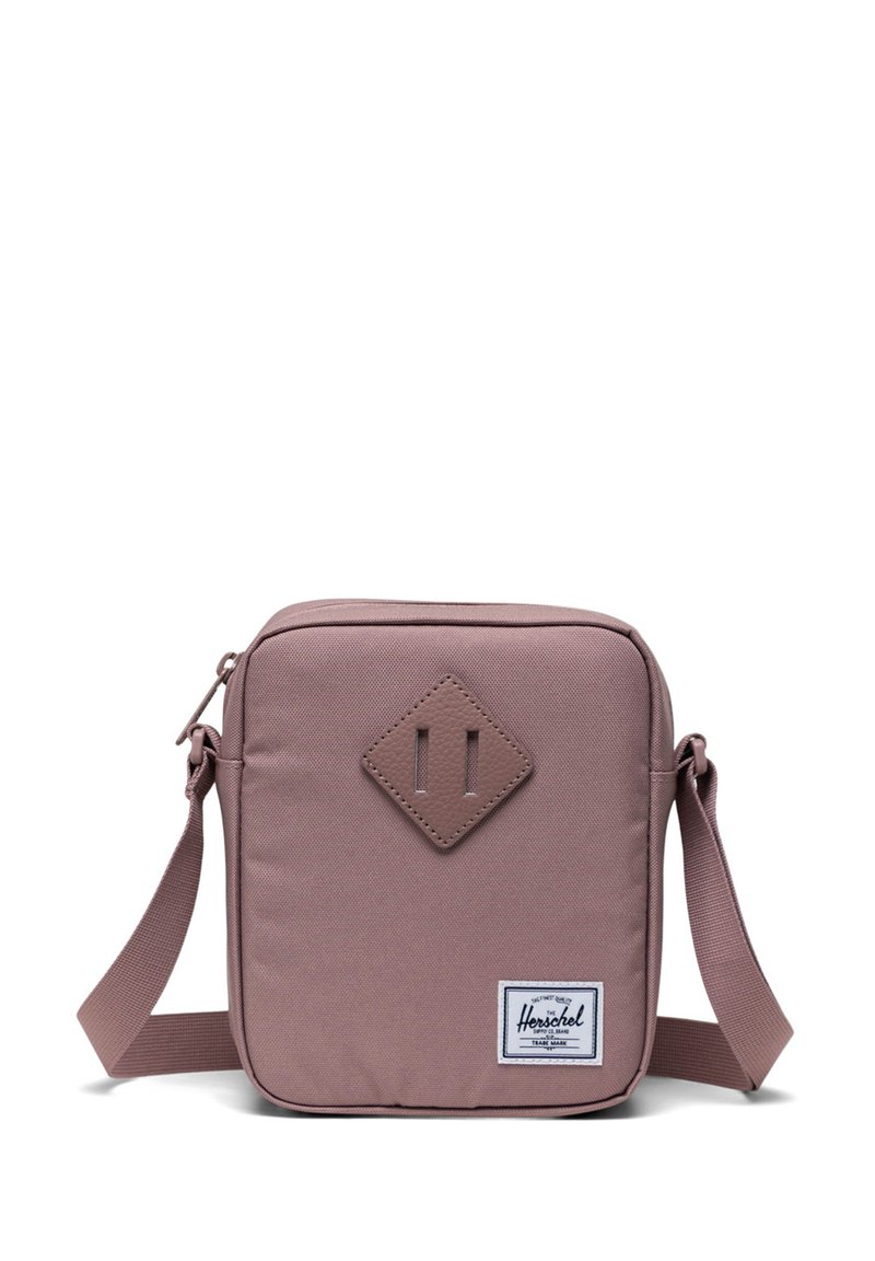 Fyrkantig, mauve crossbody-väska med en texturerad tyg, framstående diamantaccent, justerbar rem och en logotypetikett på nedersta högra hörnet.