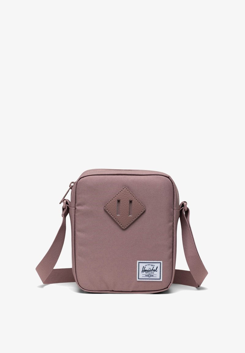 Fyrkantig, mauve crossbody-väska med en texturerad tyg, framstående diamantaccent, justerbar rem och en logotypetikett på nedersta högra hörnet.