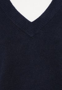 Sötétkék v-nyakú pulóver, puha kötött anyagból készült, bordázott szegéllyel a nyak körül és sima textúrával.