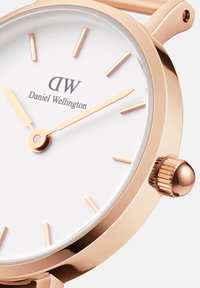 Round wristwatch with a rose gold case, white dial, and rose gold hands. Features minimalistic hour markers and a textured crown.