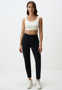 Schwarze Jogginghosen mit elastischem Bund und Kordelzug, kombiniert mit einem weißen gerippten Cropped-Top. Das Model trägt weiße Sneakers.