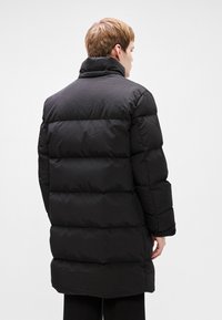 Black puffer coat with a high collar, featuring a quilted design and a hip-length cut. Smooth texture and no visible hardware.