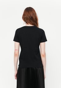 Black crew-neck T-shirt made of a smooth fabric, featuring short sleeves and a small red text detail on the upper arm.