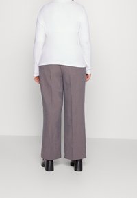 Pantalons gris à jambes larges avec une texture lisse et des plis sur le devant, associés à un haut ajusté à manches longues blanc et des bottes à talons noires.