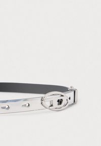 Tanek kovinski srebrn pas z ovalno oblikovano, polirano srebrno sponko na belem ozadju.