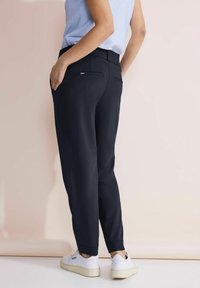 Svart skräddarsydda byxor med smal passform, med två bakfickor, kompletterat med vita sneakers och en ljusrandig topp.