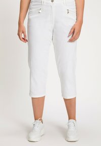 Pantaloni cropped bianchi realizzati in tessuto texturizzato, con tasche laterali con zip e chiusura con bottone. Indossati con sneakers bianche.