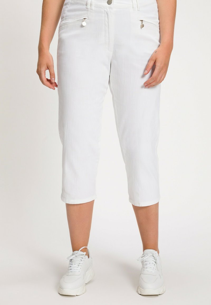 Pantaloni cropped bianchi realizzati in tessuto texturizzato, con tasche laterali con zip e chiusura con bottone. Indossati con sneakers bianche.