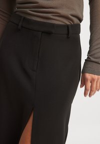 Sort nederdel lavet af glat stof, med en sideslids og en skræddersyet talje. Pyntet med en sidelomme for ekstra detalje.