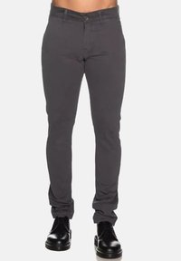 Pantaloni grigi slim-fit realizzati in un tessuto misto cotone, con chiusura a bottone, cinque tasche e una texture leggermente stropicciata. Indossati con scarpe nere.