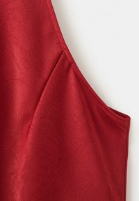 Rotes ärmelloses Kleidungsstück aus feinem, strukturiertem Stoff mit sauberer, verstärkter Naht entlang der Armöffnung und der Seitennaht.