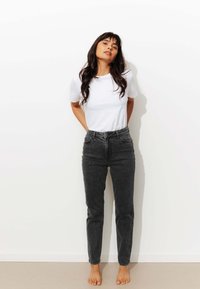 T-shirt blanc à manches courtes associé à un jean noir taille haute. Le jean présente une coupe droite et un léger délavage.