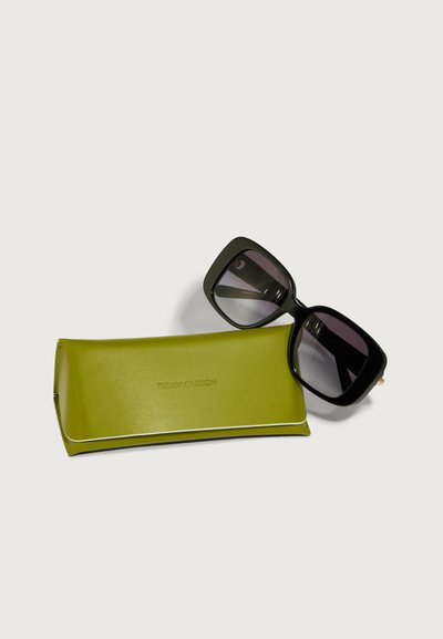 Črne oversize sončne očala z gradientnimi lečami ob limonasto zeleni trdi škatli, na kateri je vtisnjen logotip "TORY BURCH".