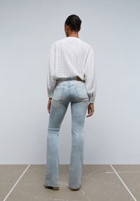 Blusa bianca in pizzo con maniche voluminose abbinata a jeans flare azzurri, caratterizzati da una vita alta e dettagli di sfumatura leggera.