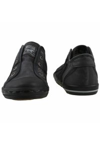Black shoes with a rubber sole, canvas upper, and metal eyelets. Features a low-top design and a textured finish. Back view shows stitching detail.