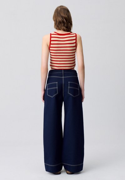 Canotta a righe rossa e crema abbinata a pantaloni larghi blu navy con tasche posteriori e cuciture a contrasto.