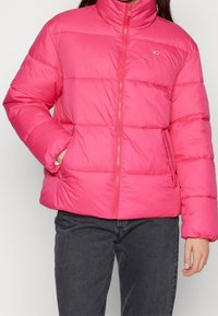 Giacca a vento rosa con colletto alto, zip frontale e polsini elasticizzati. Presenta sezioni trapuntate e tasche laterali per la funzionalità.