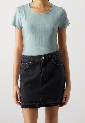 Kobieta ubrana w jasnoniebieski krótki sweter z dzianiny i wysoką, czarną dżinsową mini spódniczkę z postrzępionym dołem.