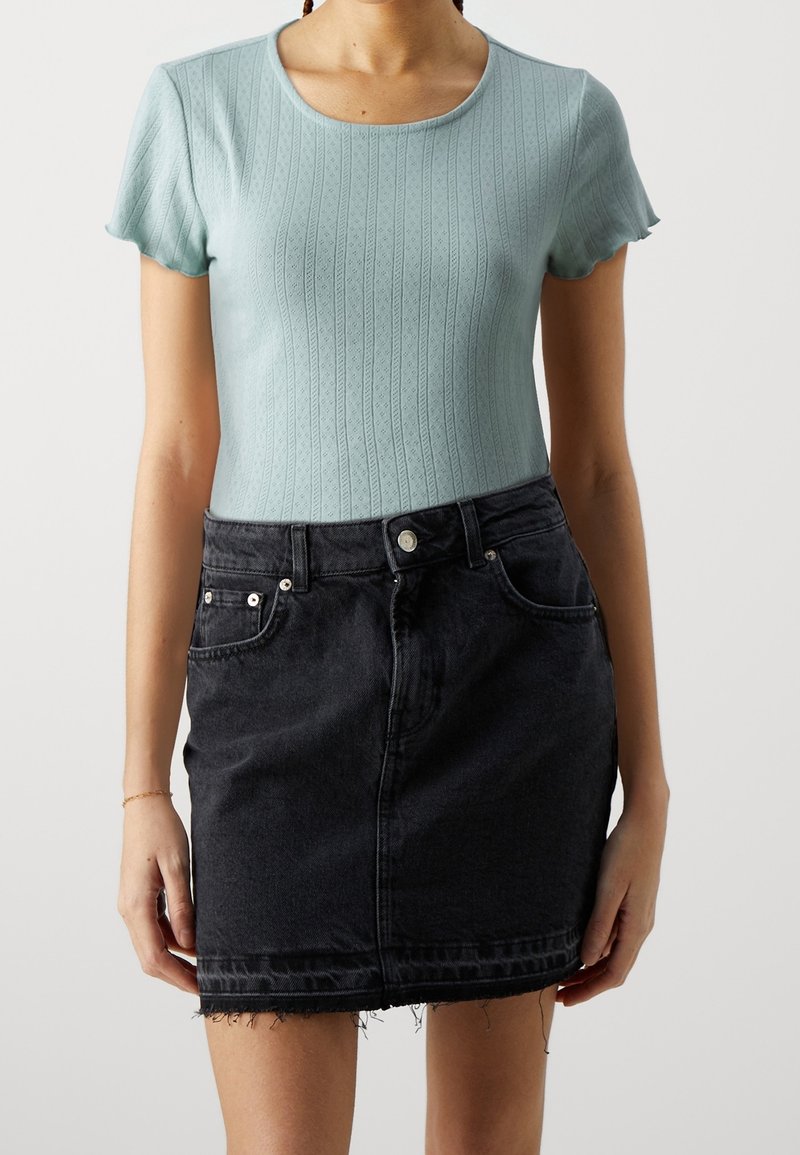 Femme portant un haut en maille bleu clair à manches courtes et une mini-jupe en jean noire taille haute avec ourlet effiloché.
