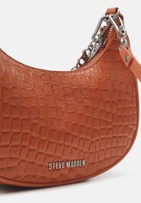 Petit sac à main marron avec texture cuir de crocodile, fermeture éclair argentée, détail chaîne et logo Steve Madden sur le devant.
